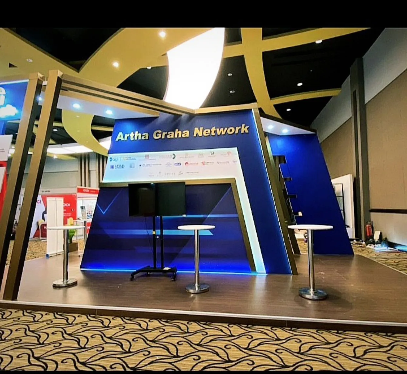 Booth pameran Artha Graha Network dengan panel biru dan rangka kayu